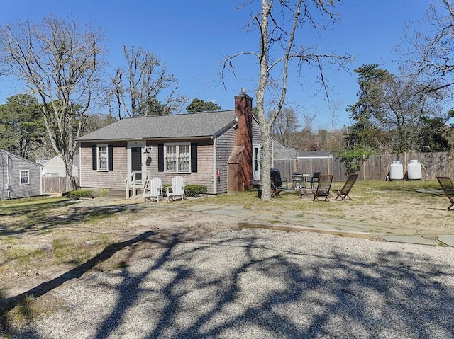 bungalow-style house with an outdoor fire pit, a chimney, and fence