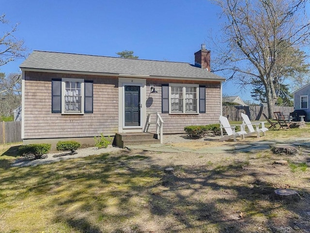 view of front of home featuring roof with shingles, a front lawn, a chimney, and fence