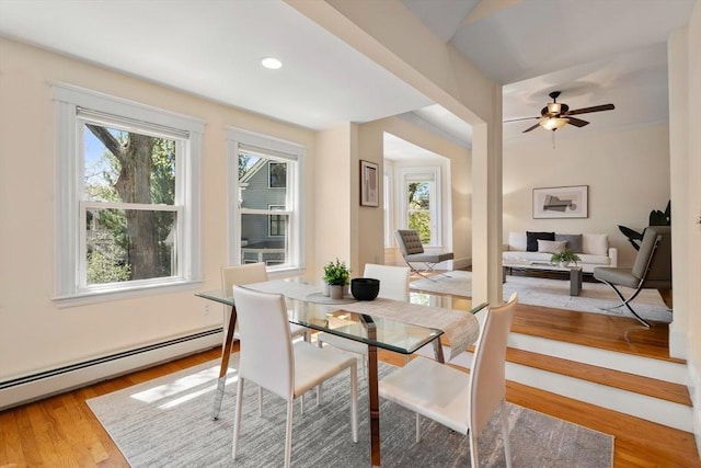 dining space with light wood-type flooring, a ceiling fan, baseboard heating, and a wealth of natural light