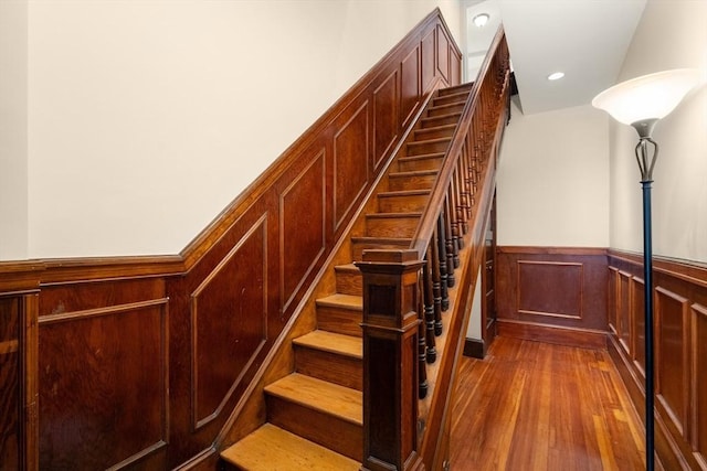 stairs with recessed lighting, wood finished floors, and a wainscoted wall