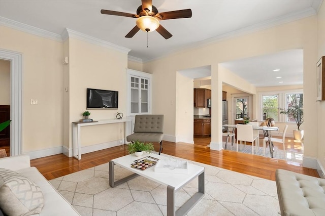living area with ceiling fan, baseboards, ornamental molding, and light wood-style flooring
