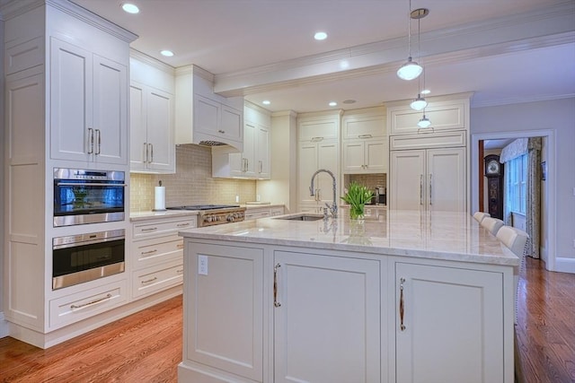 kitchen with sink, appliances with stainless steel finishes, a kitchen island with sink, and decorative light fixtures