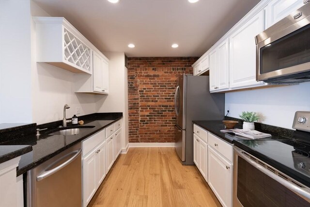 kitchen with sink, appliances with stainless steel finishes, white cabinetry, brick wall, and light wood-type flooring