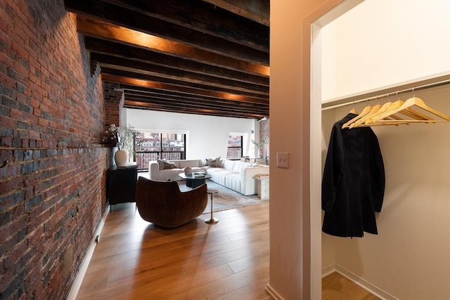 interior space with wood-type flooring, brick wall, and beam ceiling