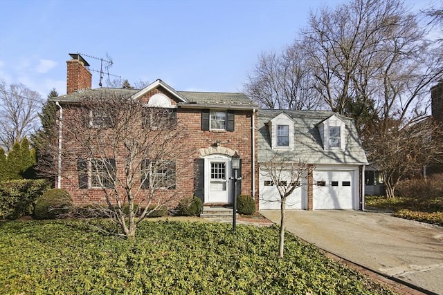 colonial house with a chimney, concrete driveway, a garage, and brick siding