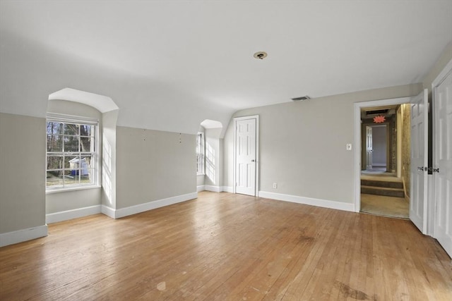 unfurnished room with light wood-type flooring, visible vents, baseboards, and vaulted ceiling