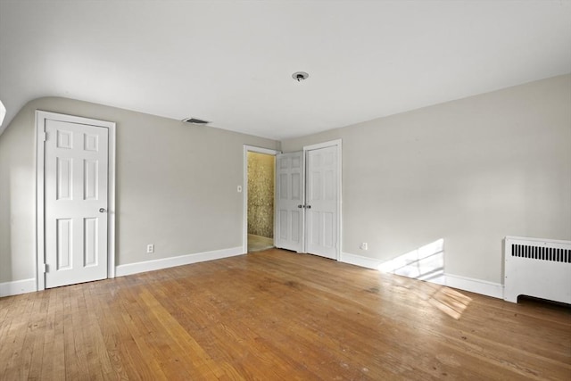 unfurnished bedroom with hardwood / wood-style flooring, radiator heating unit, visible vents, and baseboards