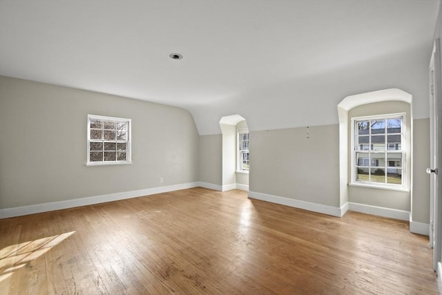 empty room featuring baseboards, lofted ceiling, arched walkways, and hardwood / wood-style floors