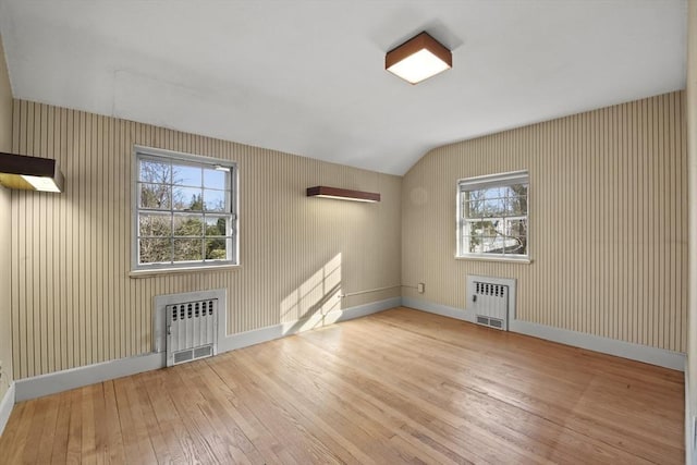 unfurnished room with lofted ceiling, radiator, baseboards, and wood-type flooring