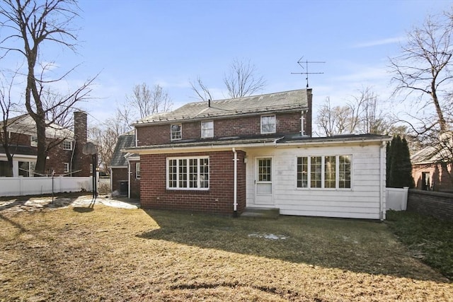 rear view of house featuring brick siding, a yard, and fence