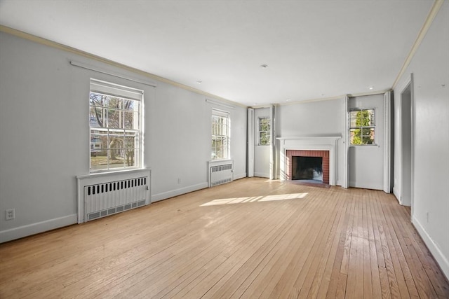 unfurnished living room featuring a brick fireplace, radiator, light wood-type flooring, and crown molding