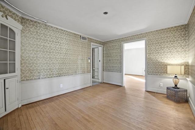 empty room with wainscoting, wallpapered walls, crown molding, and hardwood / wood-style floors