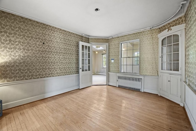 spare room with wainscoting, radiator, wallpapered walls, and wood-type flooring