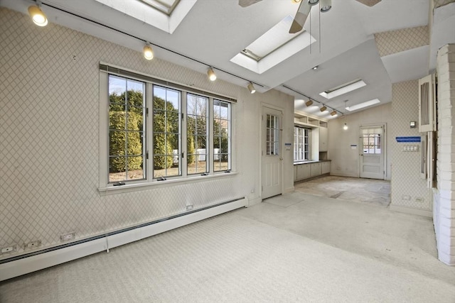 carpeted spare room with vaulted ceiling with skylight, wallpapered walls, a baseboard heating unit, and ceiling fan