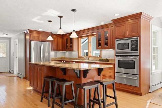 kitchen with appliances with stainless steel finishes, brown cabinetry, a warming drawer, and baseboard heating