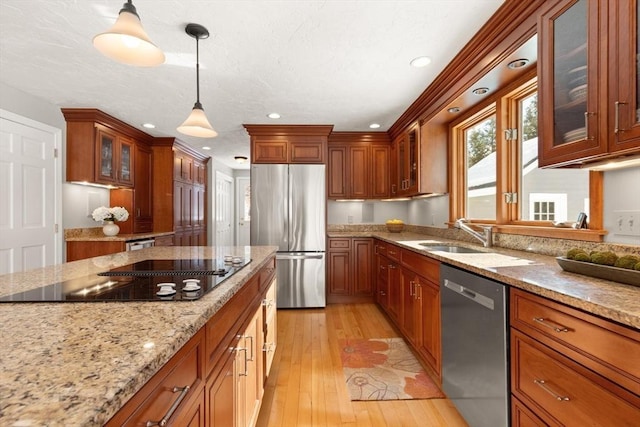 kitchen featuring light stone counters, decorative light fixtures, appliances with stainless steel finishes, light wood-style floors, and a sink