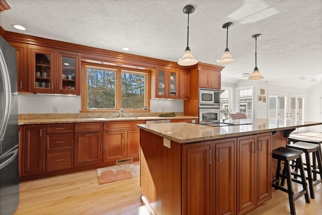 kitchen with appliances with stainless steel finishes, brown cabinetry, plenty of natural light, and light wood-style floors