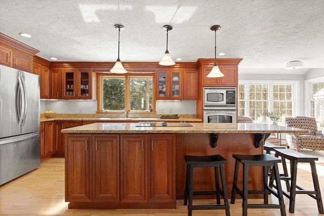 kitchen with brown cabinetry, light wood-style flooring, glass insert cabinets, a breakfast bar, and stainless steel appliances