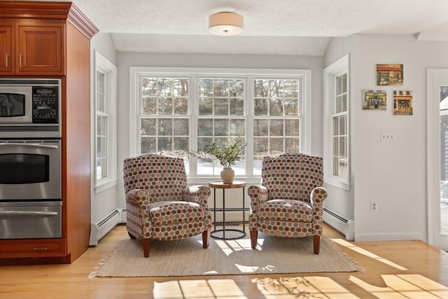 sitting room featuring a baseboard heating unit, light wood-style floors, a baseboard radiator, and a healthy amount of sunlight