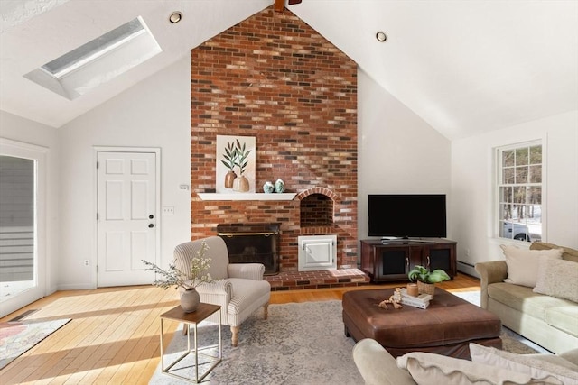 living room with high vaulted ceiling, a baseboard radiator, a skylight, wood finished floors, and a brick fireplace