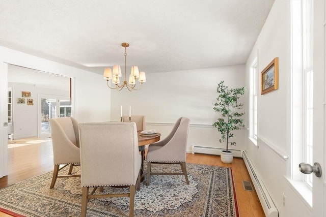 dining area with a baseboard heating unit, a chandelier, visible vents, and light wood finished floors