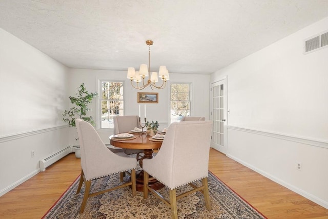 dining area featuring visible vents, light wood-style flooring, an inviting chandelier, baseboard heating, and a textured ceiling