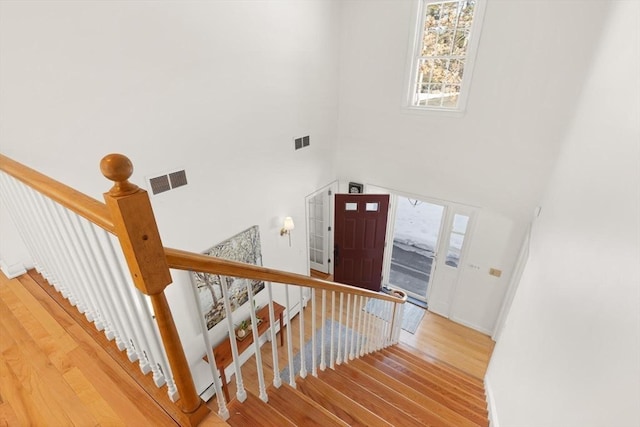 stairway featuring a high ceiling, wood finished floors, and visible vents