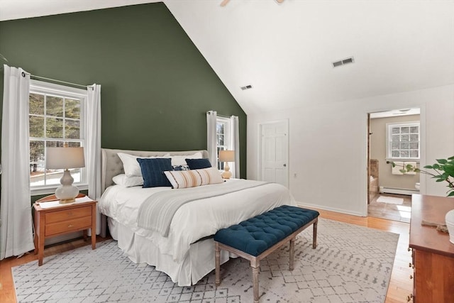 bedroom with light wood finished floors, baseboards, visible vents, baseboard heating, and high vaulted ceiling