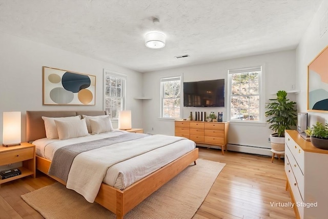 bedroom featuring a textured ceiling, multiple windows, a baseboard radiator, and light wood-style flooring