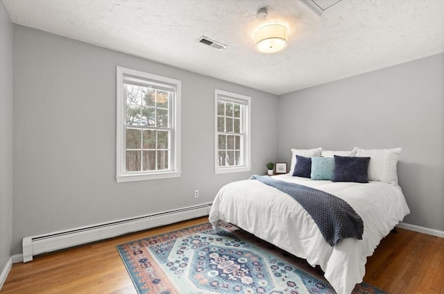 bedroom featuring baseboards, visible vents, wood finished floors, a textured ceiling, and a baseboard heating unit