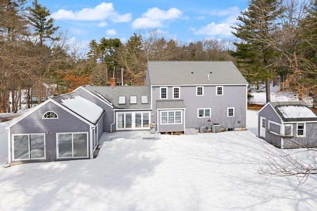 snow covered house with a garage, french doors, and a chimney