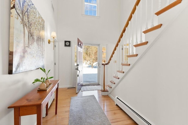 entryway with a baseboard heating unit, a high ceiling, wood finished floors, and stairs