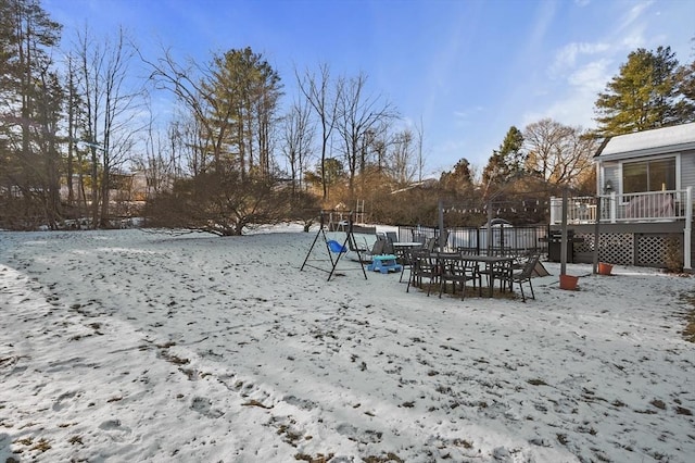 yard covered in snow featuring a playground and a wooden deck