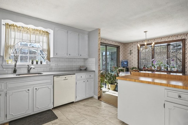 kitchen with an inviting chandelier, white cabinetry, decorative light fixtures, dishwasher, and sink