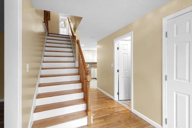 stairway with a textured ceiling, baseboards, and wood finished floors