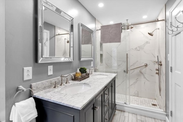 bathroom featuring a marble finish shower, recessed lighting, double vanity, and a sink