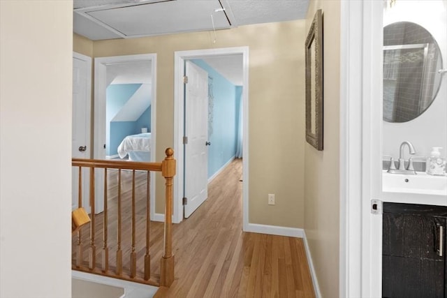 corridor featuring light wood-style flooring, attic access, baseboards, and a sink