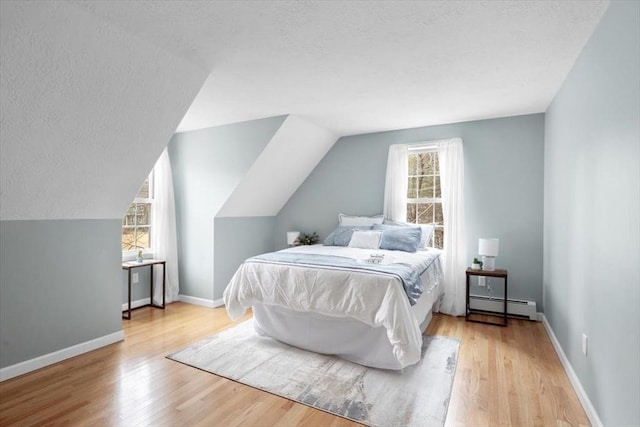 bedroom featuring a textured ceiling, a baseboard heating unit, and wood finished floors