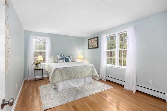 bedroom featuring a baseboard heating unit, baseboards, and light wood-style flooring