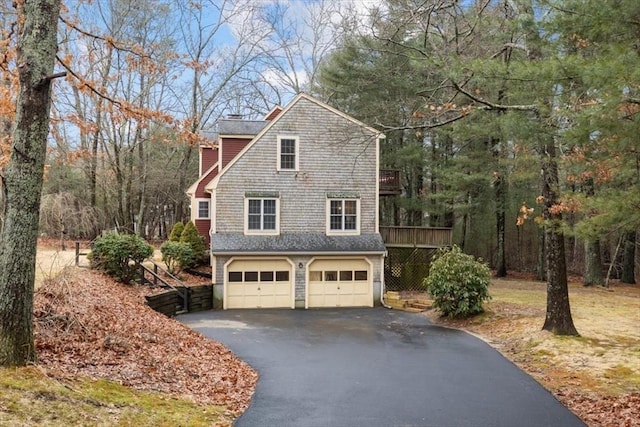 view of side of home featuring aphalt driveway, a wooden deck, a garage, and a chimney