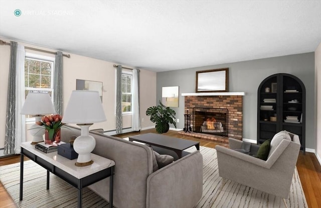 living area with a baseboard radiator, baseboards, a brick fireplace, and wood finished floors