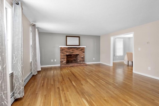 unfurnished living room featuring a baseboard heating unit, light wood-style flooring, a fireplace, and baseboards