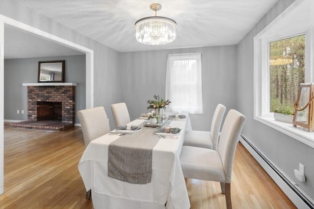 dining room with a notable chandelier, wood finished floors, a fireplace, a baseboard radiator, and baseboards