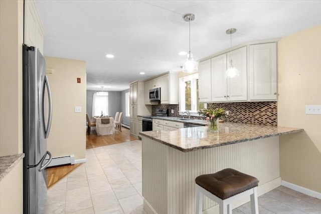 kitchen with a peninsula, a sink, appliances with stainless steel finishes, a kitchen bar, and backsplash