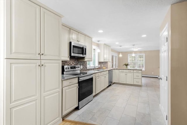 kitchen featuring a sink, appliances with stainless steel finishes, a peninsula, decorative backsplash, and baseboard heating