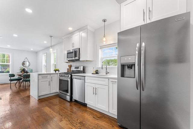 kitchen featuring appliances with stainless steel finishes, a peninsula, a sink, dark wood-type flooring, and plenty of natural light