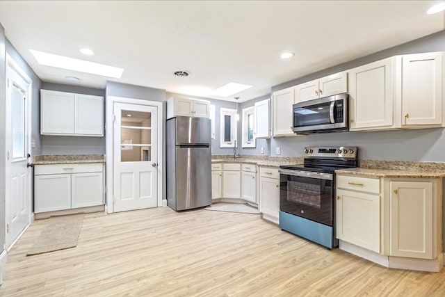 kitchen featuring white cabinetry, a skylight, light wood-type flooring, stainless steel appliances, and light stone countertops