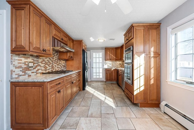 kitchen featuring decorative backsplash, appliances with stainless steel finishes, a baseboard radiator, and light stone counters