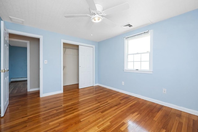 unfurnished bedroom featuring a closet, a baseboard radiator, ceiling fan, and hardwood / wood-style flooring