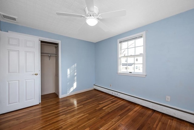 unfurnished bedroom featuring dark wood-type flooring, a closet, ceiling fan, and a baseboard heating unit